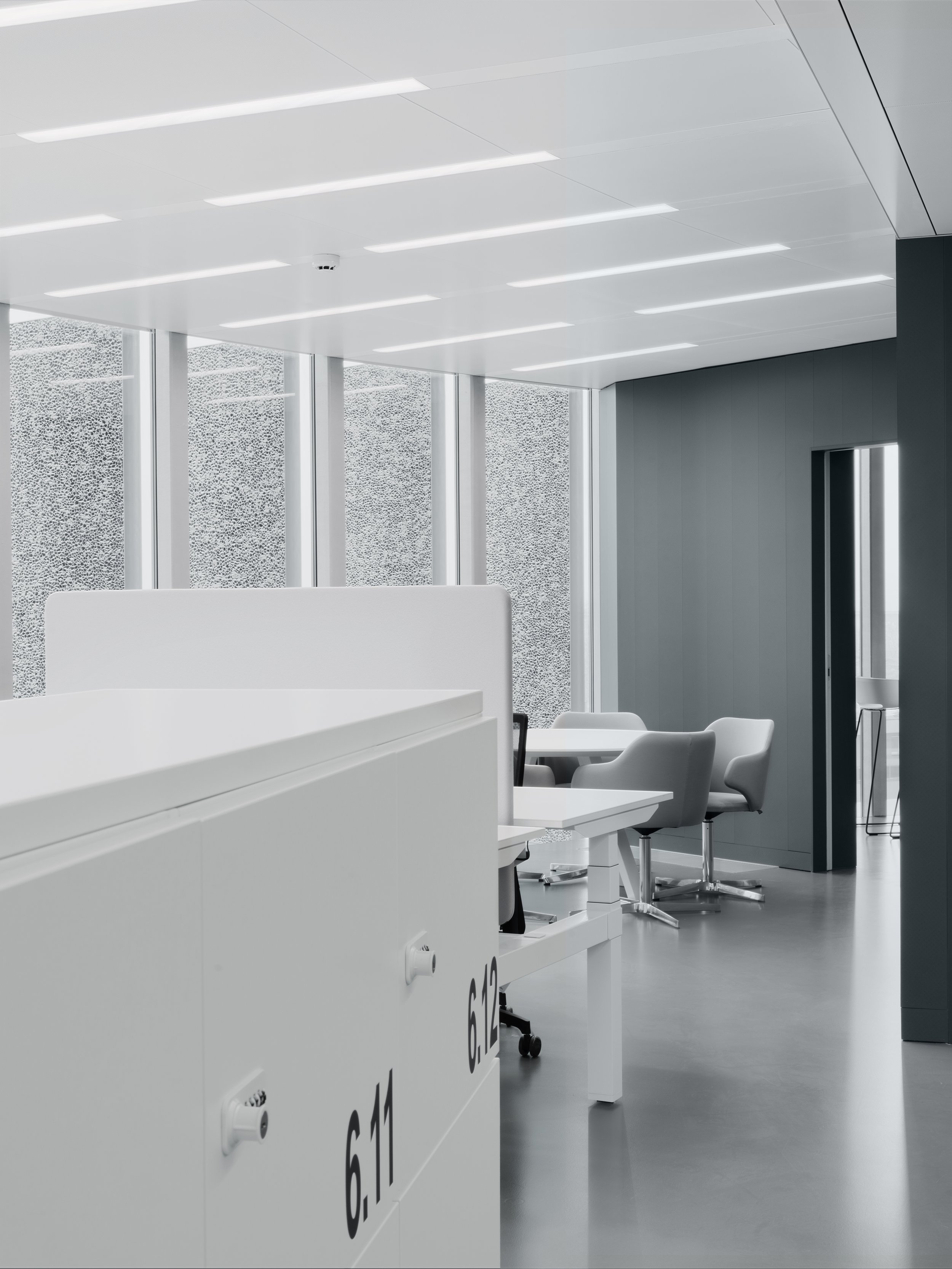 Interno di un laboratorio biomedico con apparecchiature e sedie bianche. Pareti e soffitto di colore bianco e tecnico. Puntatore a un lato.