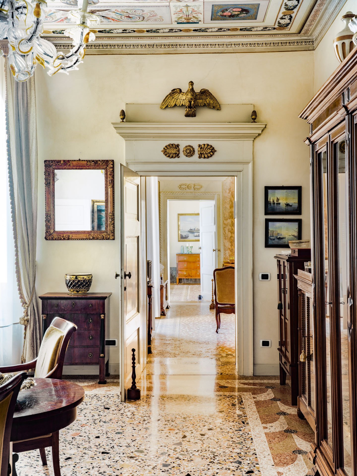 Interno di una casa elegante con arredamento classico, pareti chiare, soffitto decorato, mobili in legno scuro, quadri appesi e illuminazione elegante.