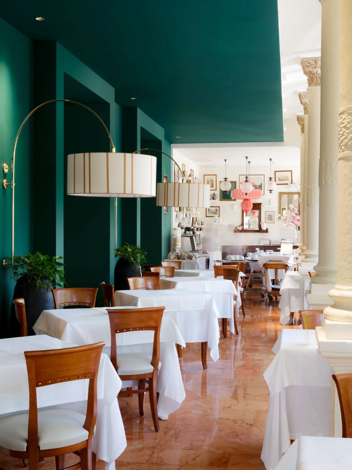 Interno di un ristorante con tavoli coperti da tovaglie bianche, sedie di legno e illuminazione soffusa, decorazioni artistiche alle pareti e colonne.
