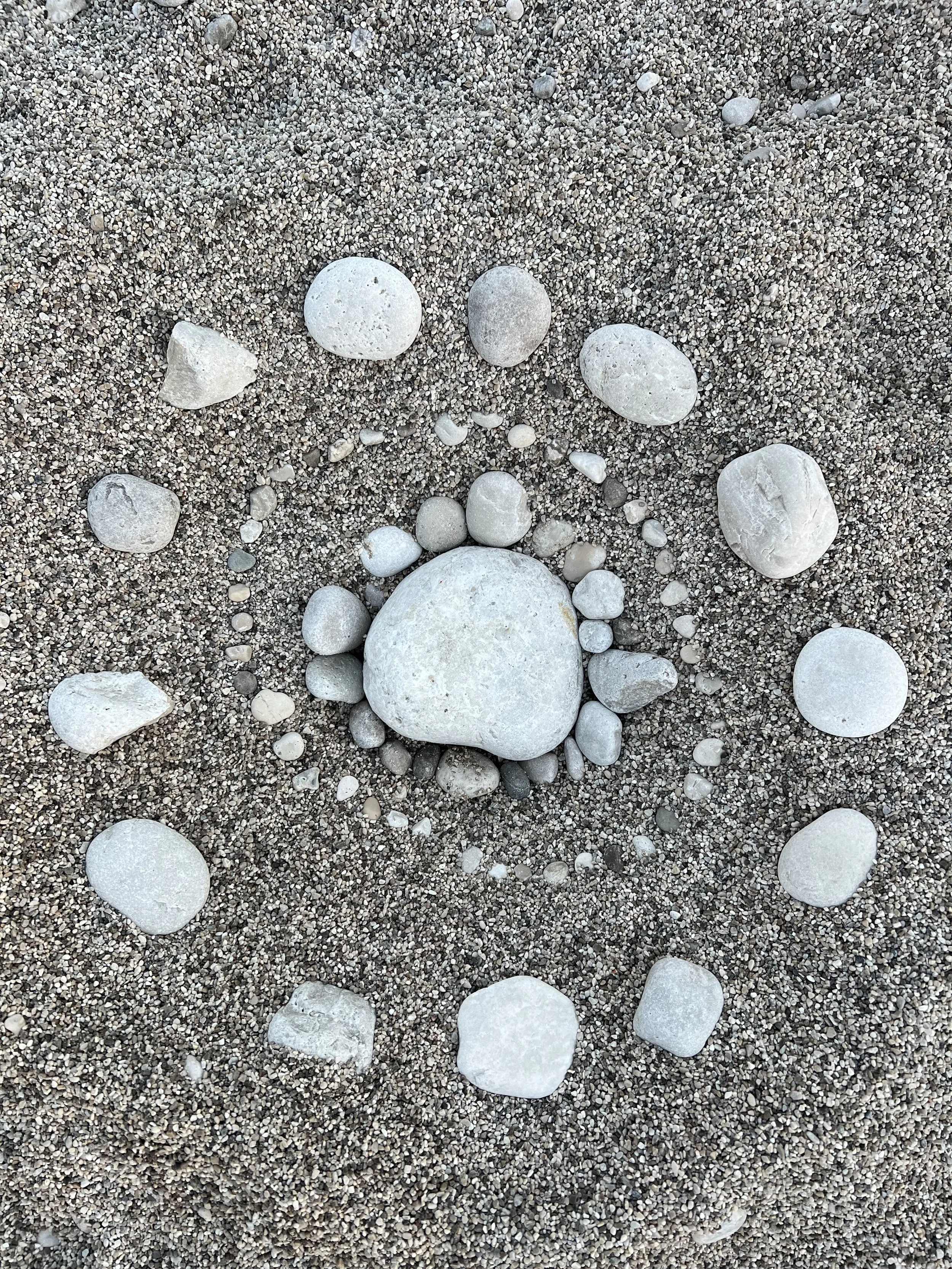 Arrangement of white and gray stones on sandy ground, with larger stones forming a semicircle at the bottom center.