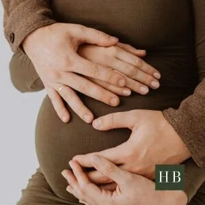Two parents' hands resting together on a pregnant belly
