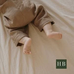 Baby legs in brown linen lying on a plain cream sheet