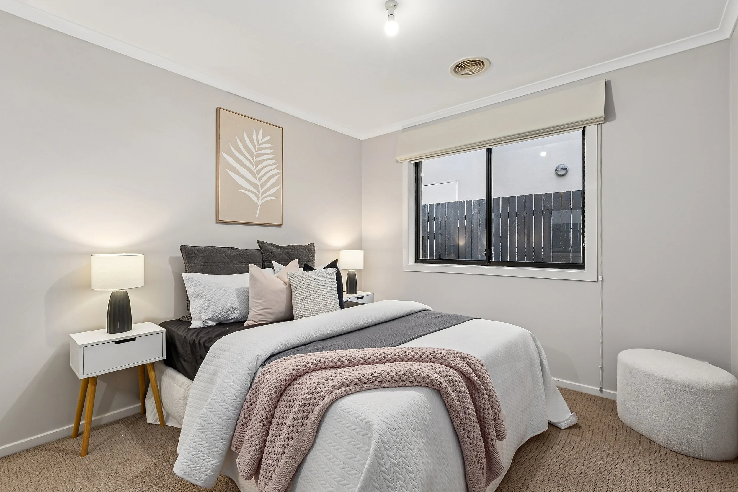 A bedroom with a bed, nightstands with lamps, a window, and a decorative wall art over the bed.
