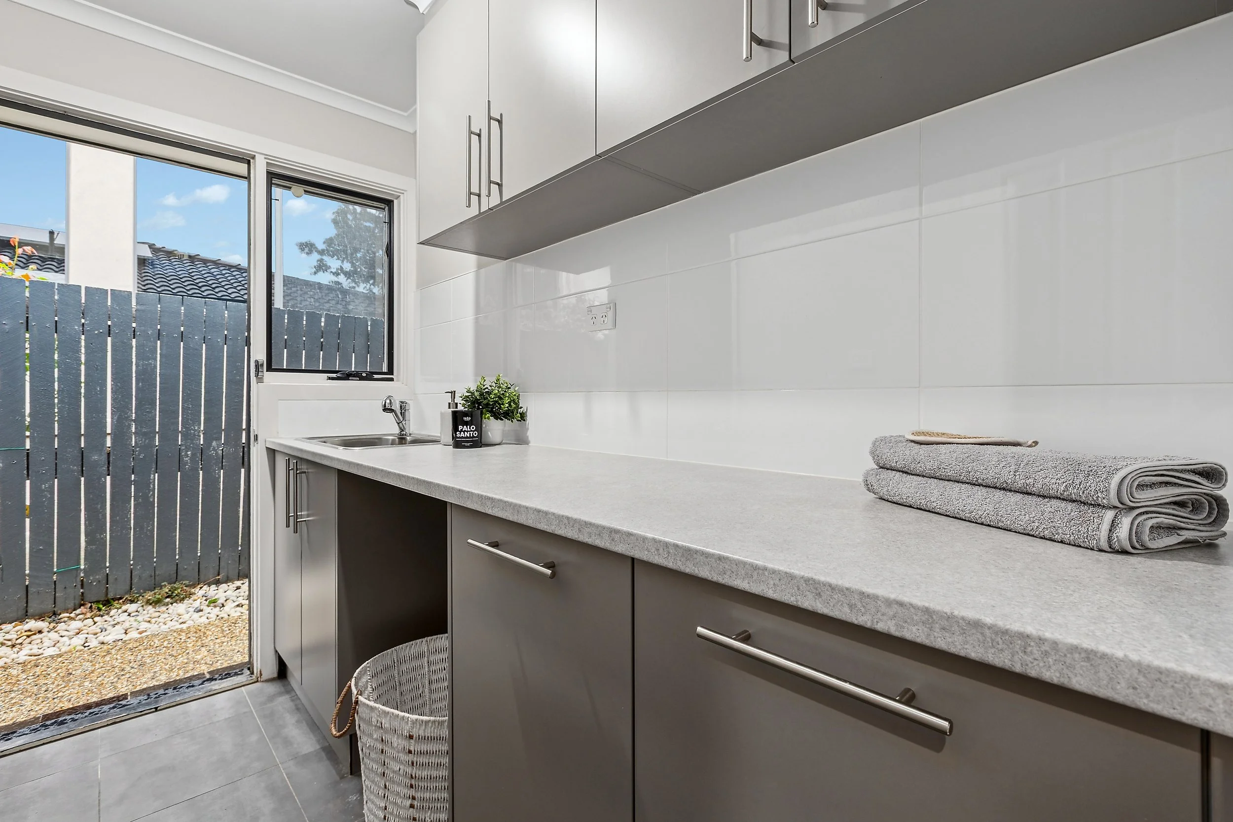 Laundry or utility room with gray cabinets, white countertop, and a window showing an outdoor view, with folded towels and a small plant on the counter.