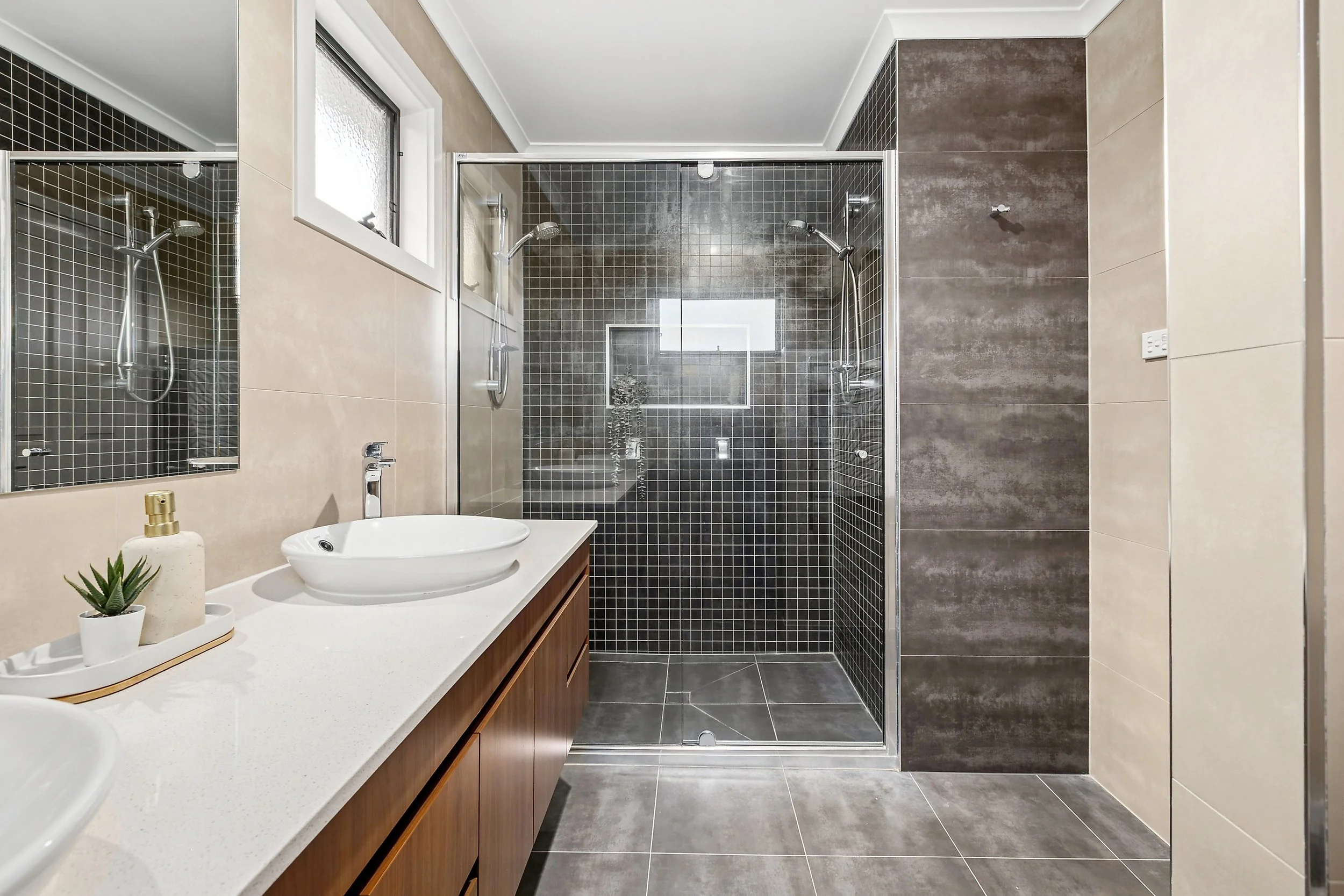 Modern bathroom with double shower, white countertop with sink, mirror, and decorative plant.
