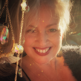 A woman smiling in sunlight with jewelry and sunlight reflections around her.