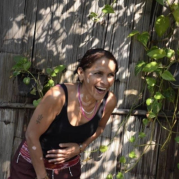 Woman laughing outdoors near wooden fence with green plants