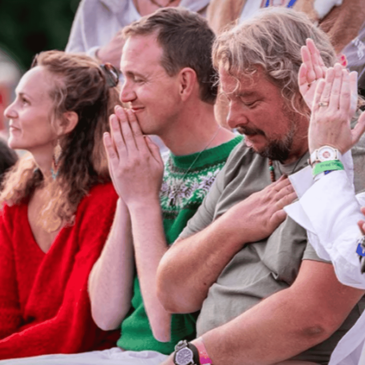 People praying at an outdoor event, some with hands clasped or on their chests in a moment of prayer or reflection.