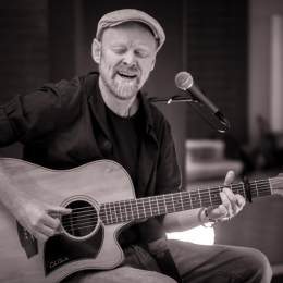 A man playing an acoustic guitar and singing into a microphone.