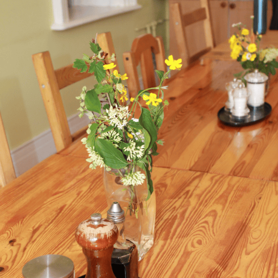 A wooden dining table with small vases containing yellow and white flowers, along with salt and pepper shakers and other table decor.