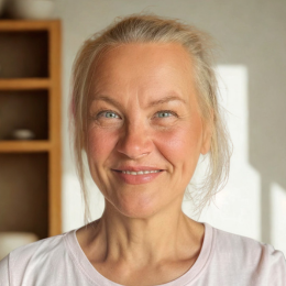 Close-up of a woman with blond hair smiling at the camera, in a well-lit room.
