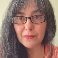 Close-up photo of a woman with long black hair, wearing glasses and a red patterned top.