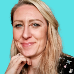 Close-up portrait of a woman with long blonde hair, smiling and looking at the camera, with a teal background.