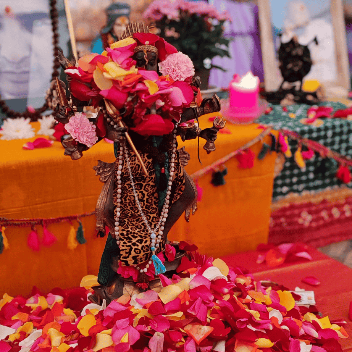 Hindu deity statue decorated with rose petals, with flowers, candles, and colorful decorations surrounding it on an altar.