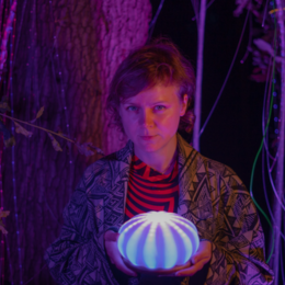 A young boy holding a glowing, striped orb in a dark, forest-like setting with purple lighting.