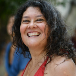 A woman with curly dark hair smiling outdoors.