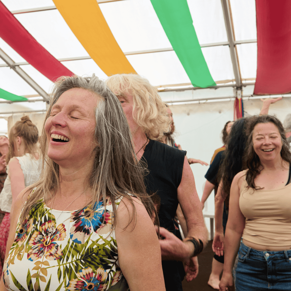 People dancing and smiling inside a decorated tent with colorful streamers.