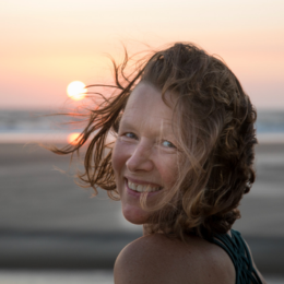 Woman with curly hair smiling at sunset on the beach.