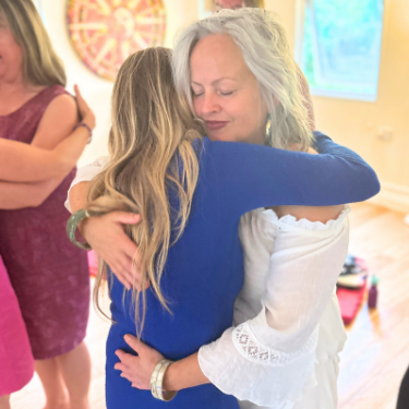 A woman with gray hair hugging a young girl indoors with other people in the background.