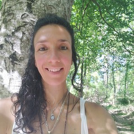 A woman taking a selfie outdoors near a tree with green leaves, smiling at the camera.