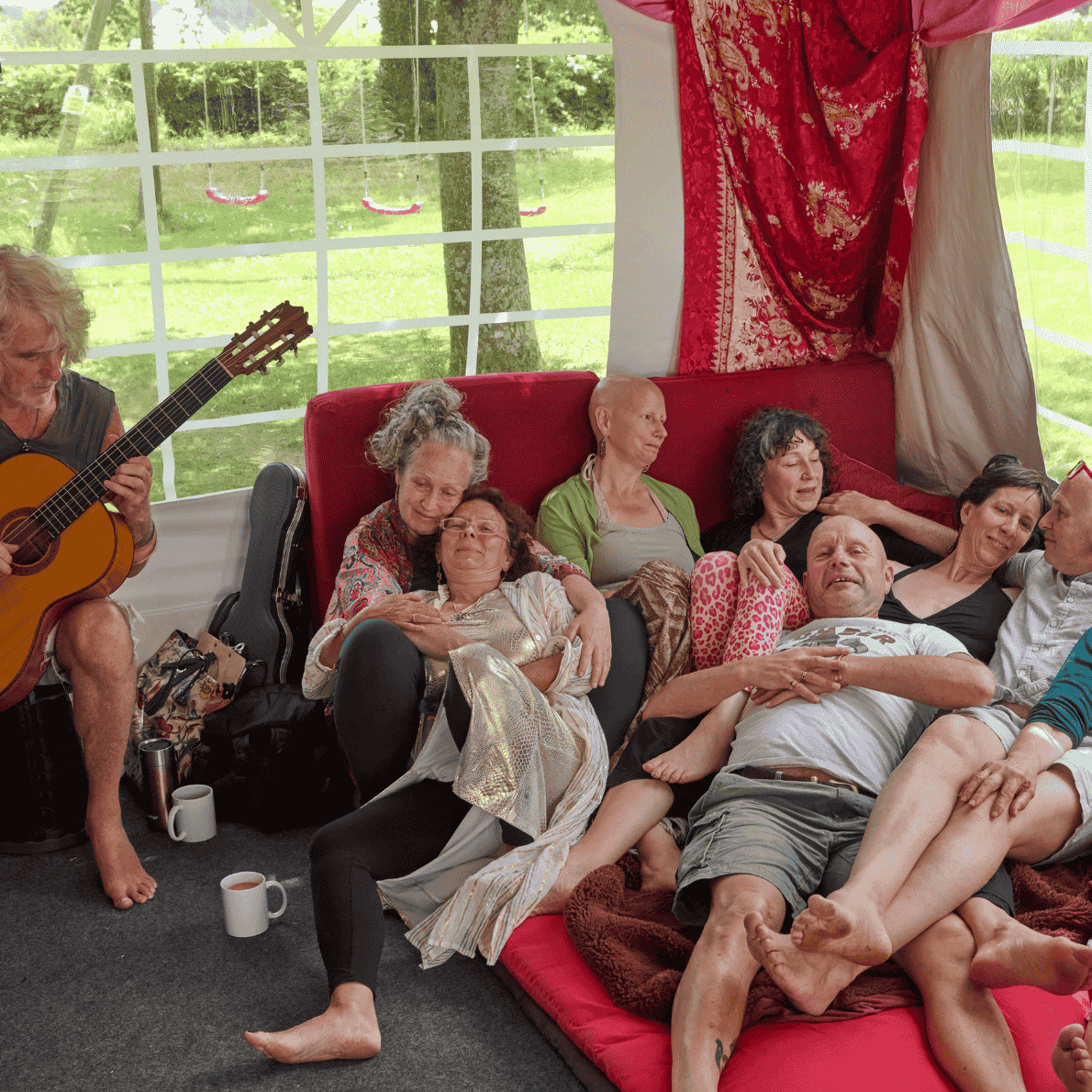 Group of people relaxing and enjoying music inside a bright tent with a view of green trees outside.