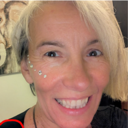 Close-up of a smiling woman with short blonde hair and decorative rhinestones on her face.