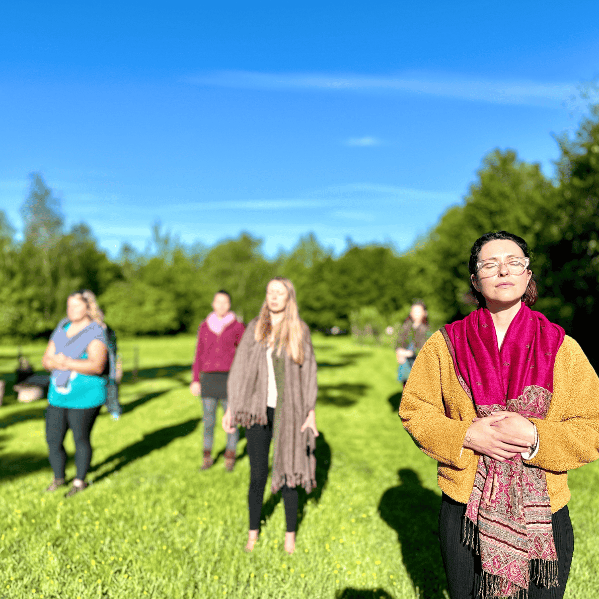 Group of women meditating outdoors on a sunny day by the trees.