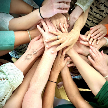 Multiple hands reaching toward a central object, possibly a balloon or ball, symbolizing teamwork or unity.