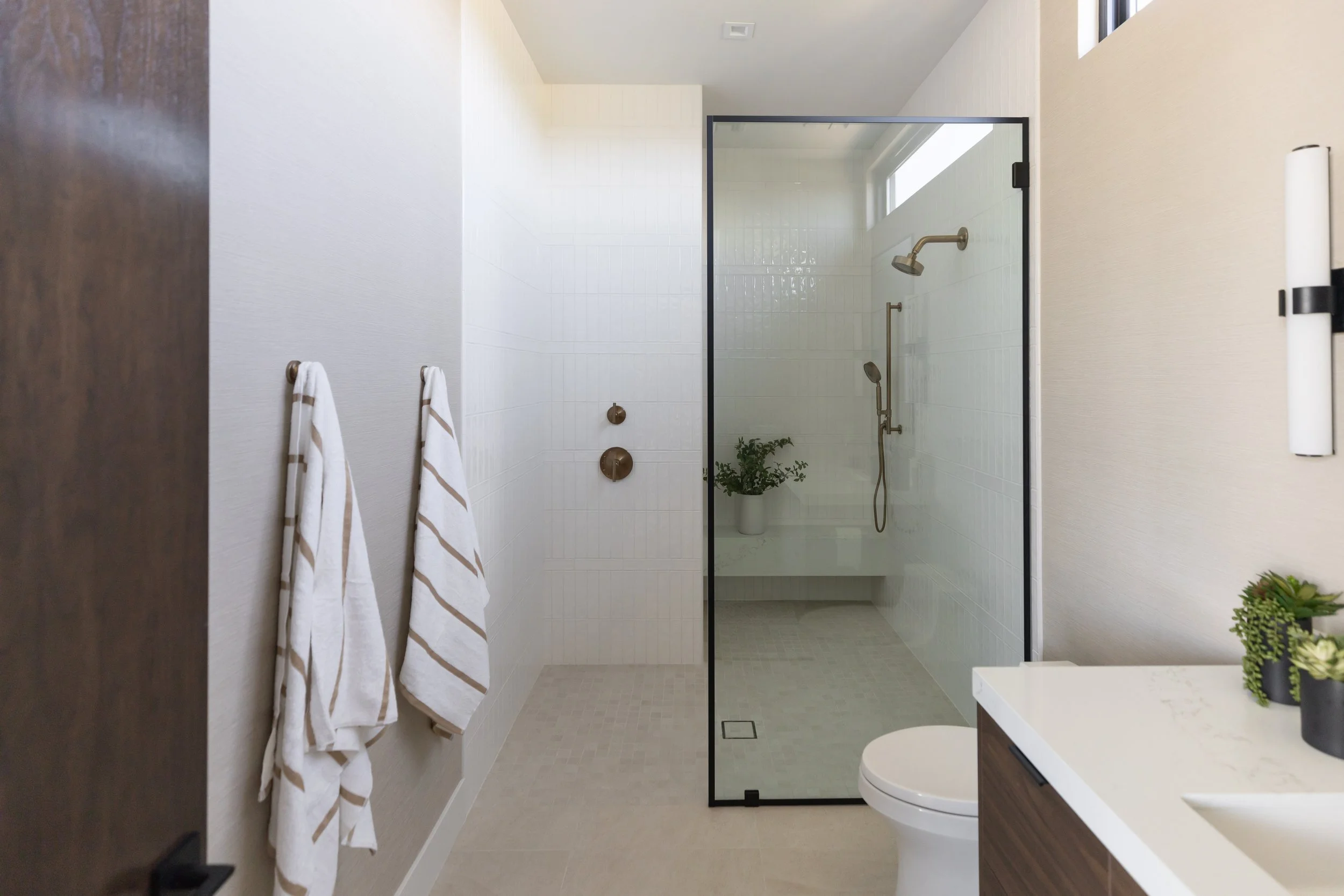 Modern bathroom with glass walk-in shower, white tile, warm wood vanity and brass fixtures in a Scottsdale custom home.