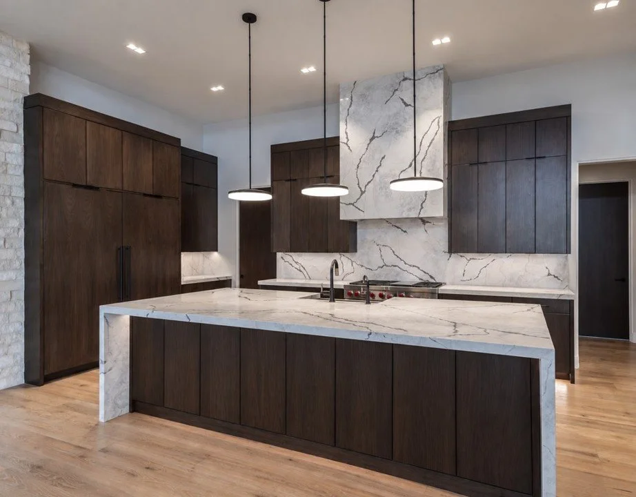 Contemporary custom home kitchen with dark wood cabinetry, veined stone countertops, and pendant lighting designed by Ashley Marie Interiors.