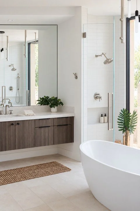 Modern primary bathroom featuring floating wood cabinetry, freestanding bathtub, and glass shower in a custom home.
