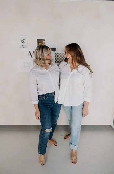 Two members of the Ashley Marie Interiors team smiling together in their design studio in Scottsdale, Arizona.