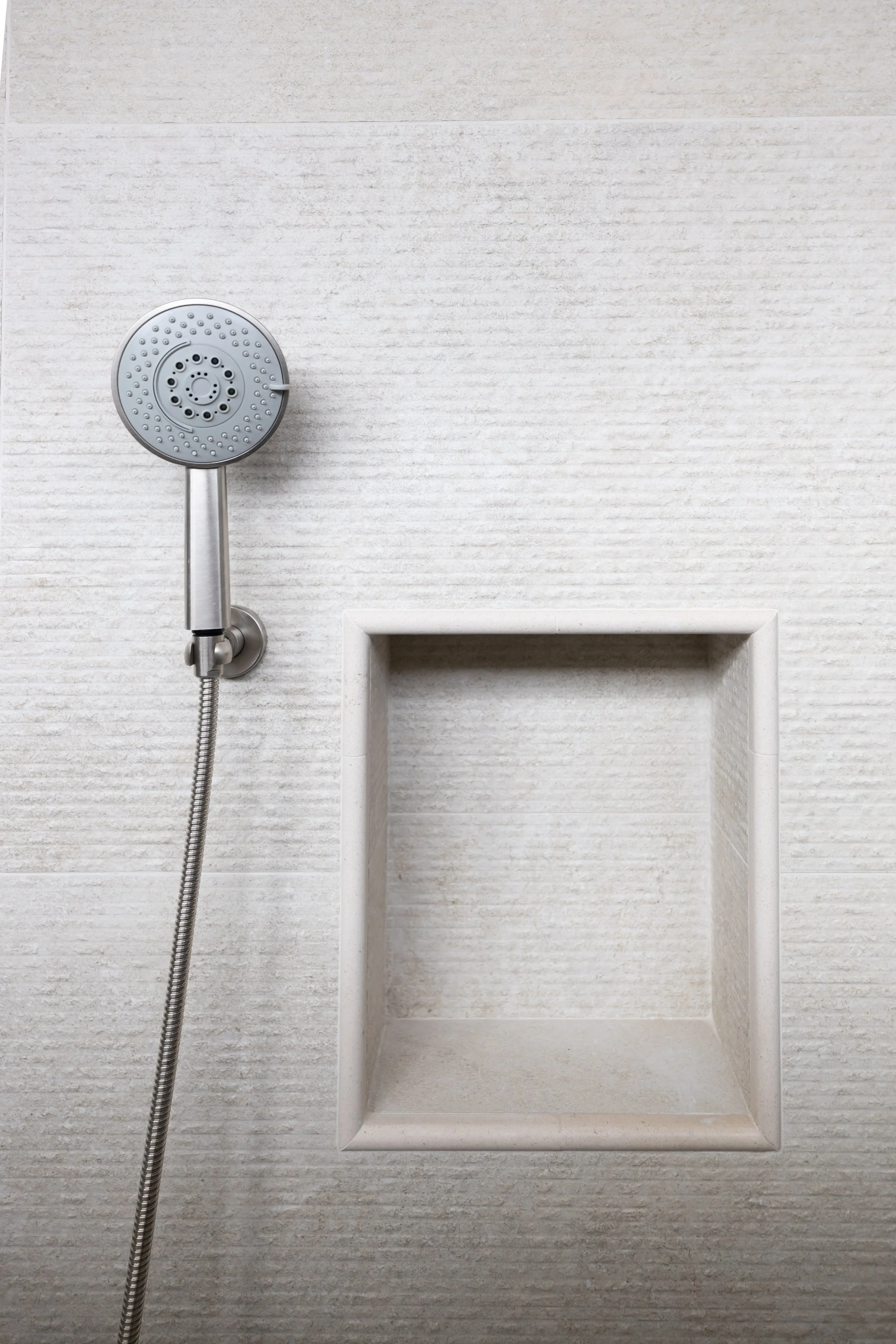 Custom shower niche with textured neutral tile and handheld shower fixture in a Scottsdale home