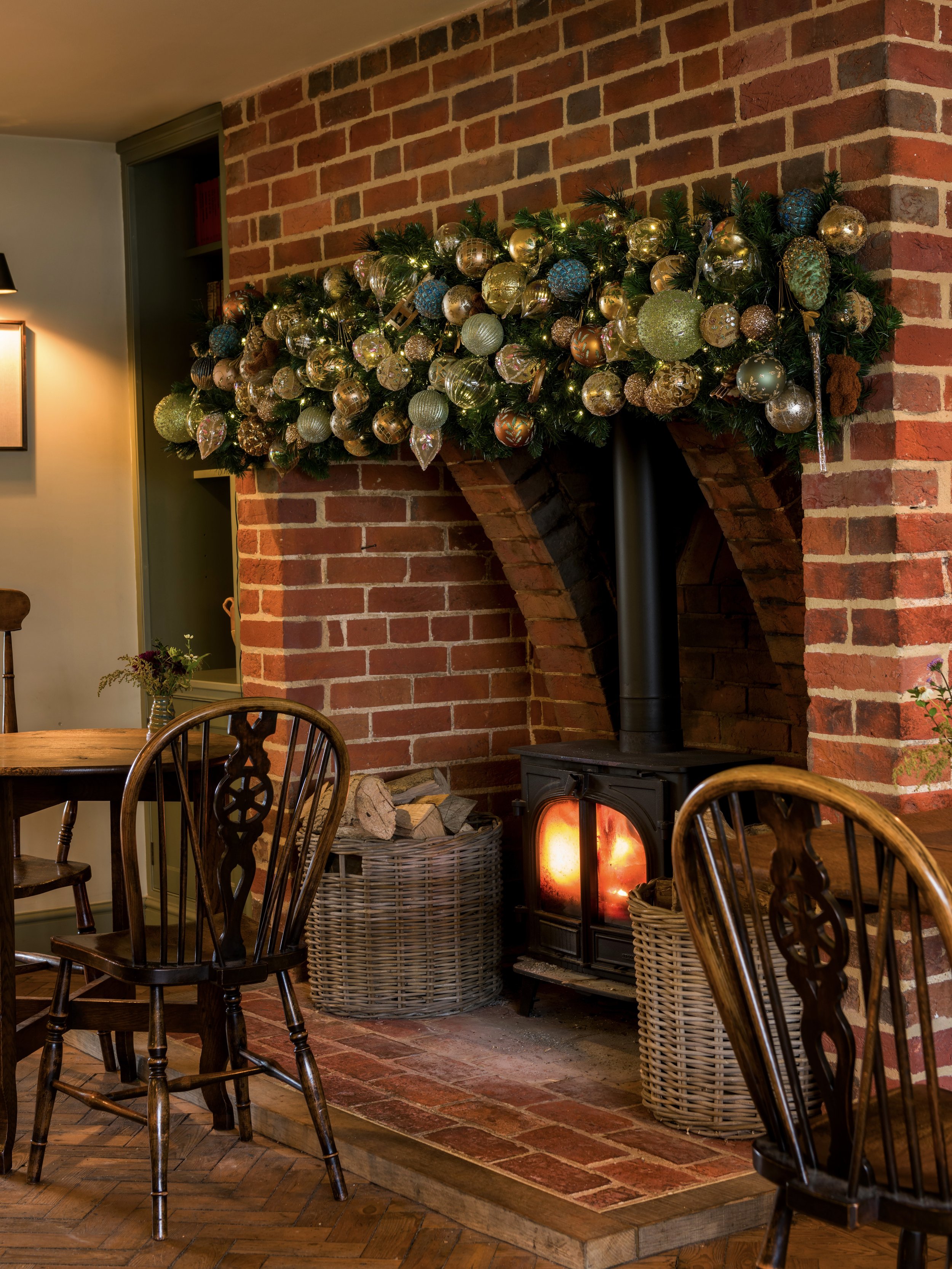 Cozy brick fireplace with a roaring wood-burning stove and festive bauble garland at The Woodcote.