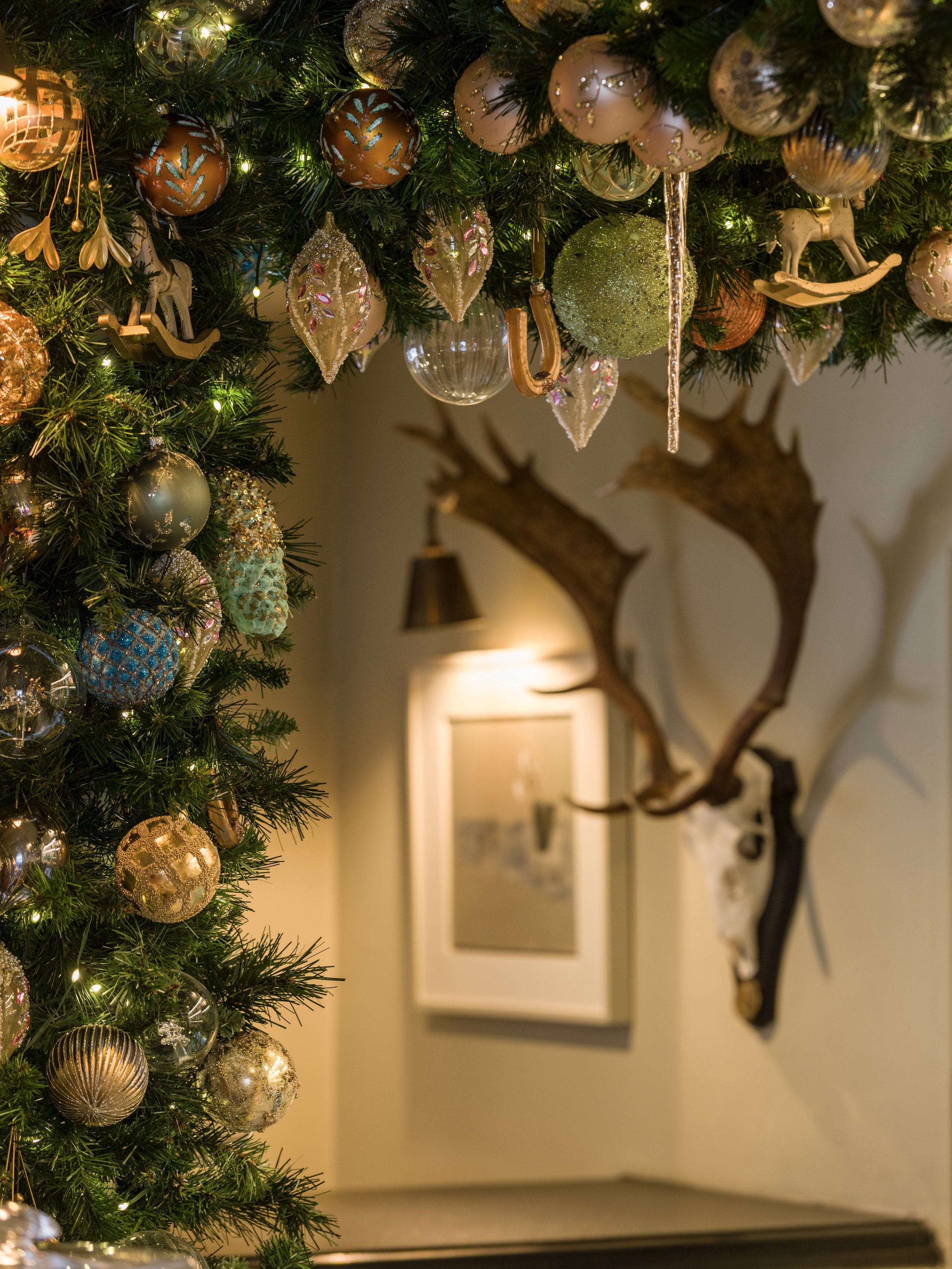 Detail of a luxury festive garland with gold and green baubles next to a stag antler mount at The Woodcote.
