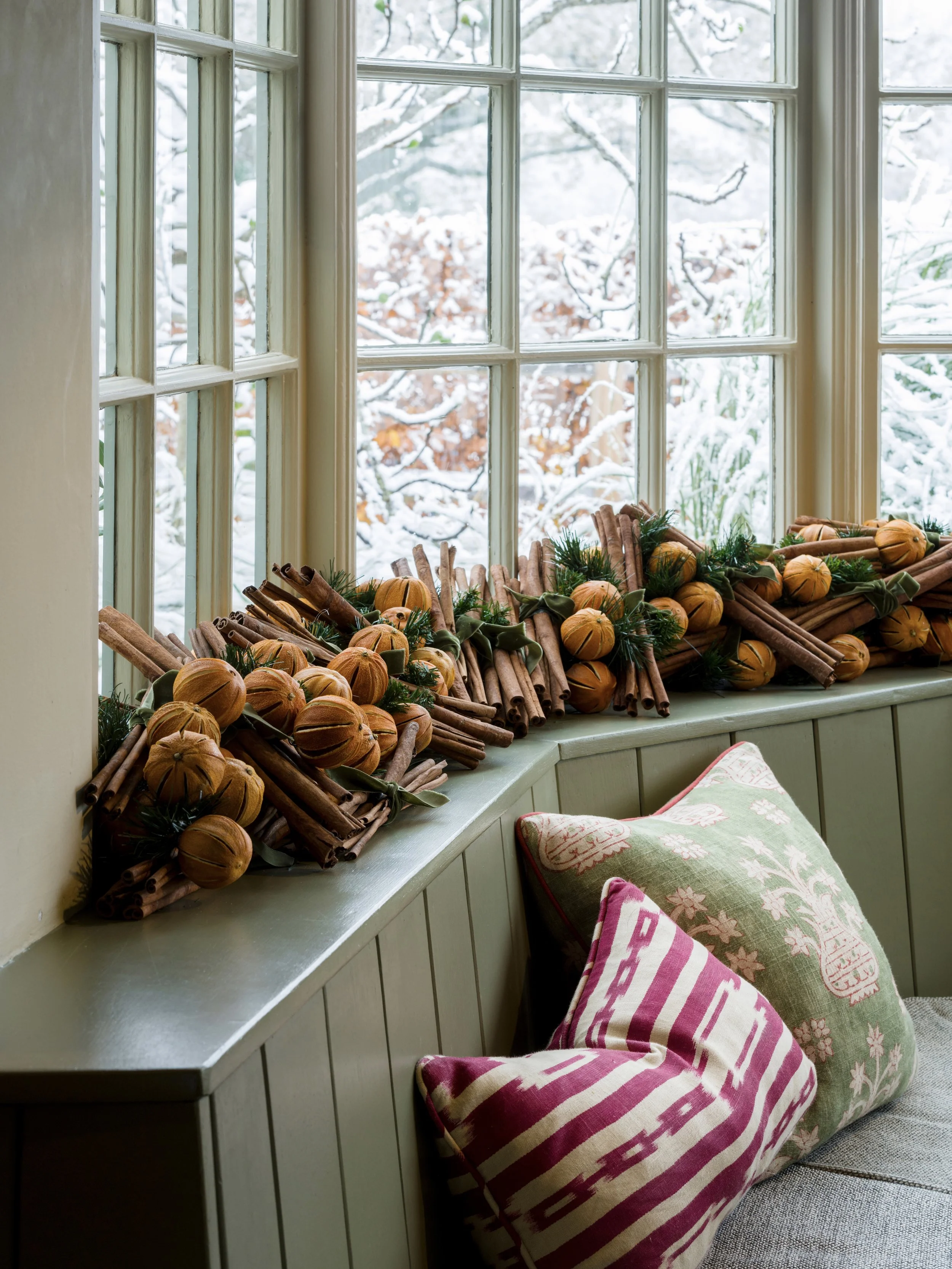 Cozy window seat at The Woodcote decorated with dried oranges and cinnamon sticks, overlooking a snowy winter garden.