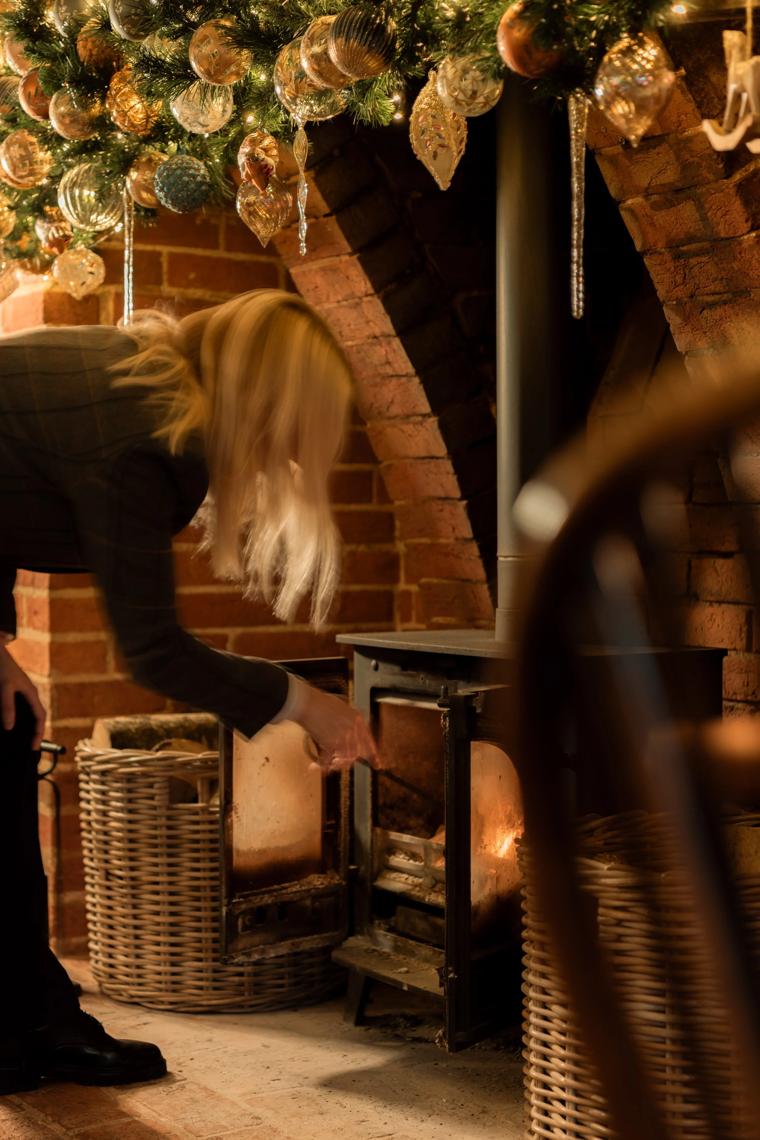 A member of The Woodcote team tending the wood-burning stove beneath festive decorations in Graffham, West Sussex.