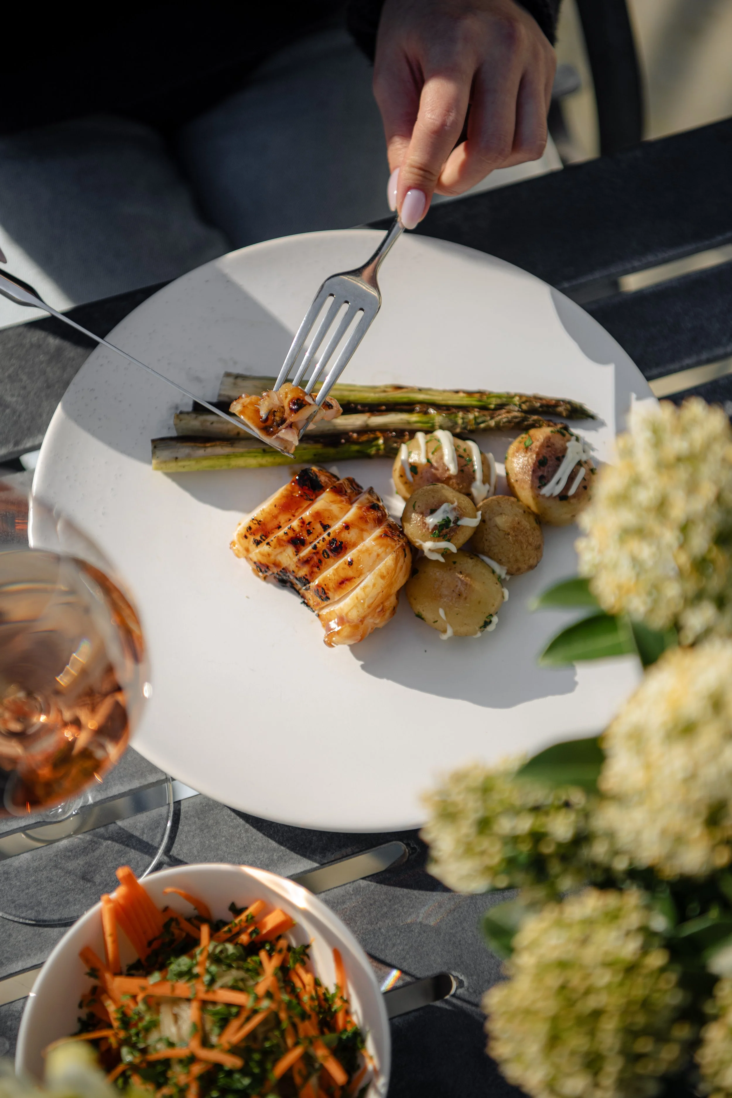 Grilled chicken breast served with charred asparagus and baby potatoes on a white plate, enjoyed on The Woodcote's outdoor terrace with a glass of rosé wine.