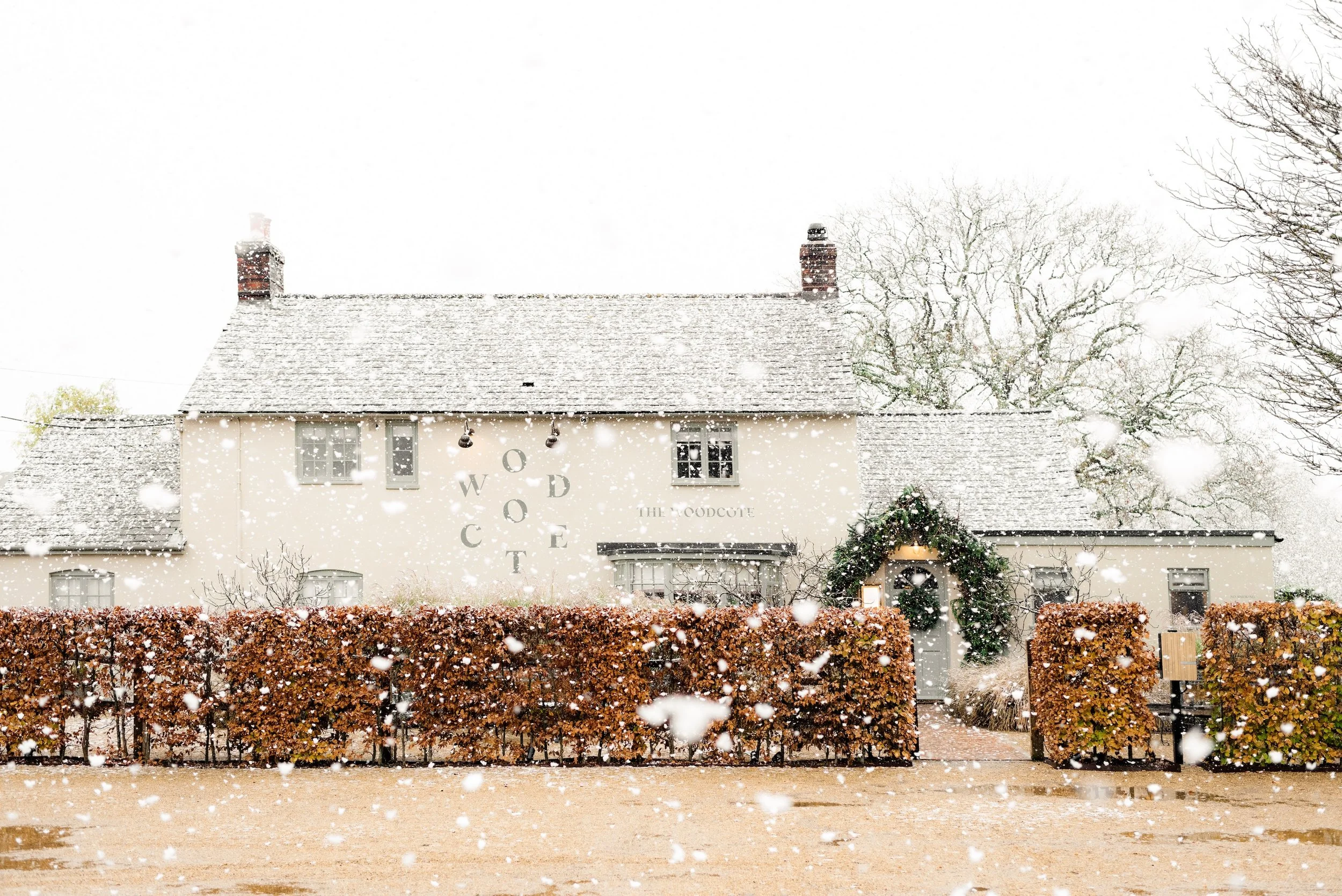 Snow falling over The Woodcote exterior and Christmas-decorated entrance in Graffham, West Sussex.