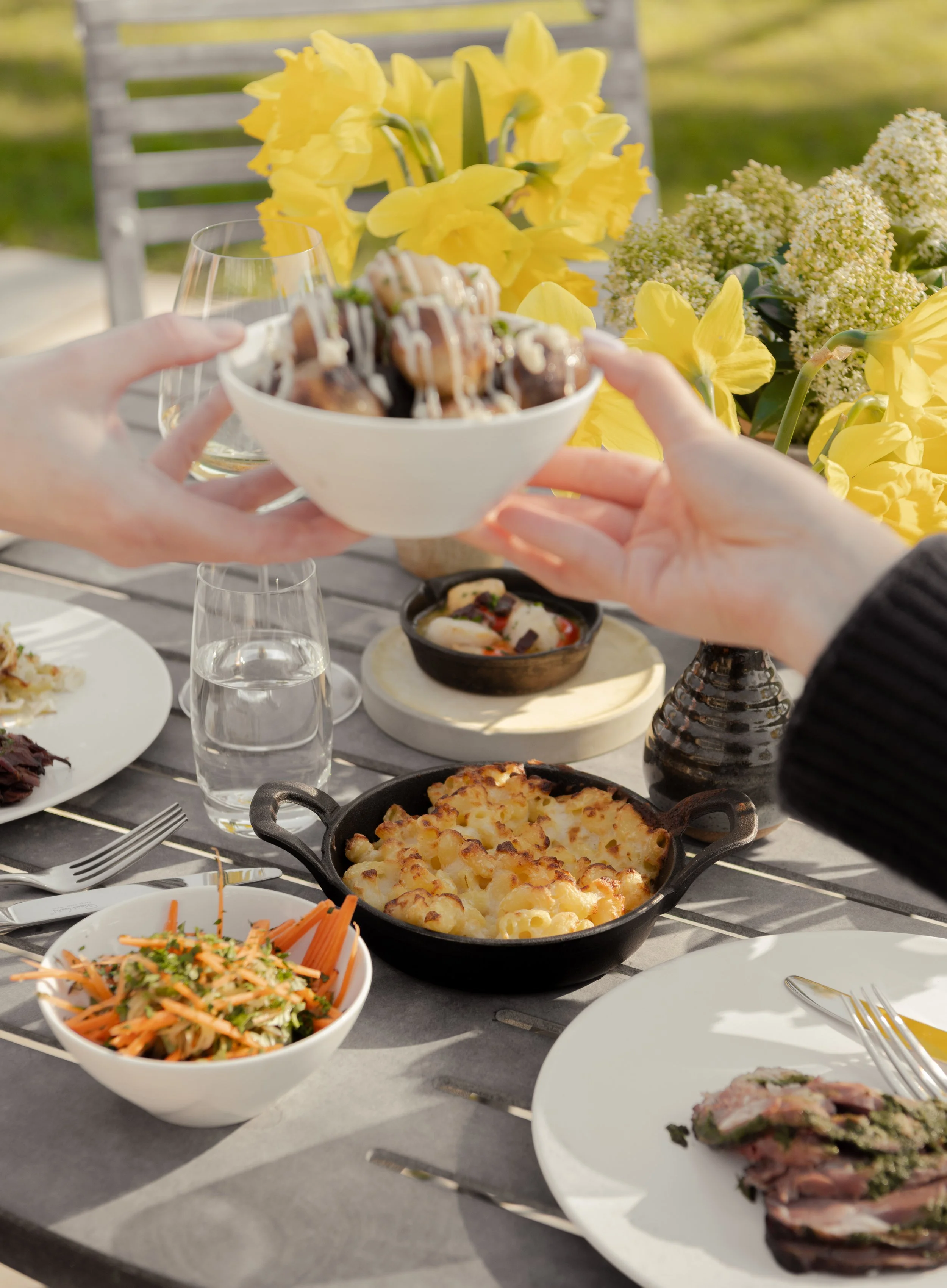 Friends sharing a festive Easter Sunday lunch at The Woodcote with fresh yellow daffodils, mac and cheese, and seasonal spring dishes.