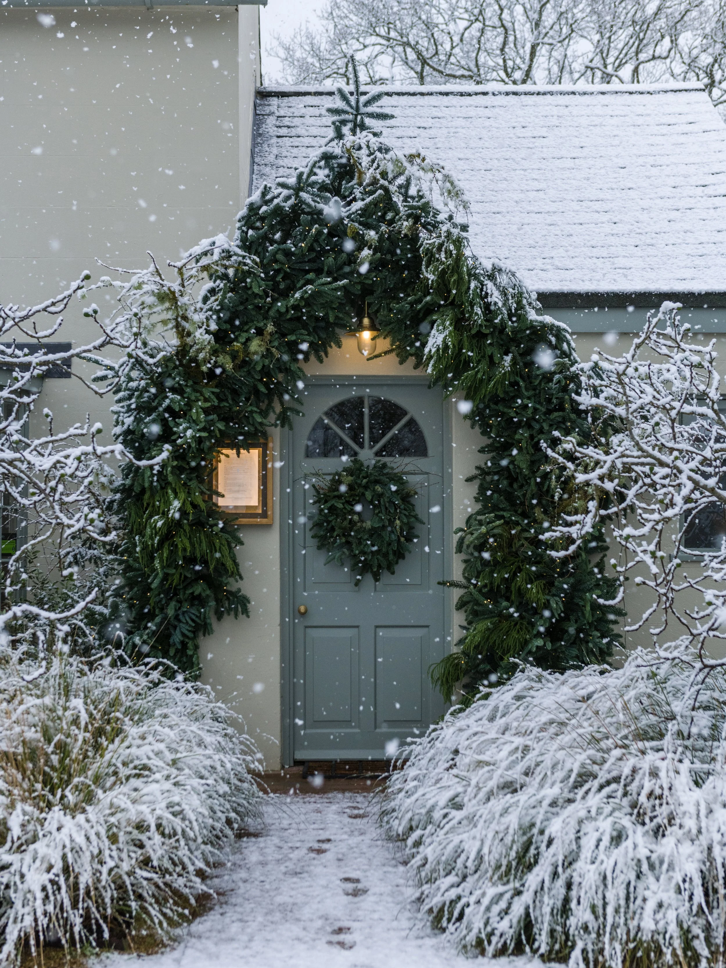 The snow-covered entrance of The Woodcote decorated with a festive evergreen arch and wreath.