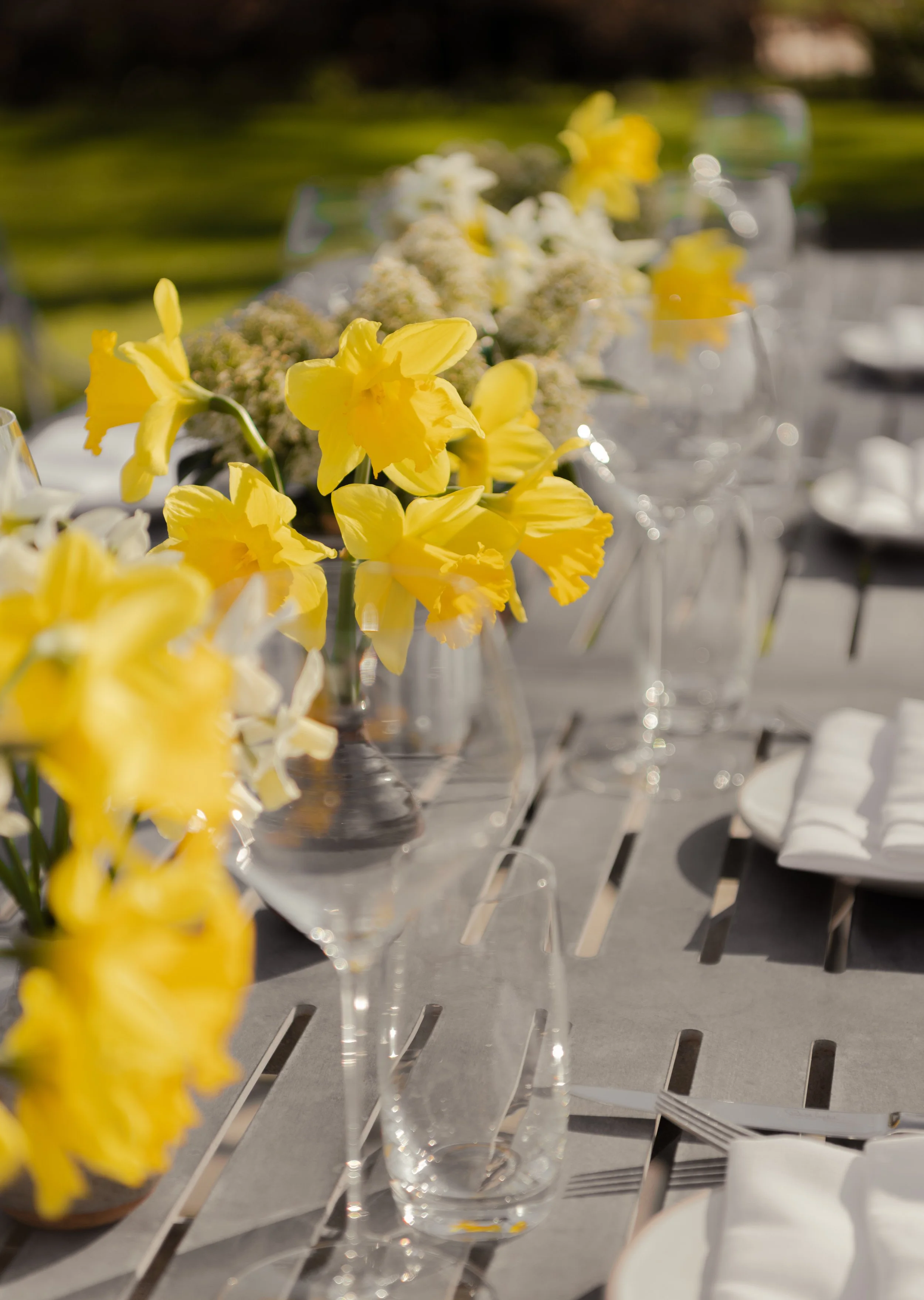 Beautifully set outdoor dining table at The Woodcote with yellow daffodils, white spring flowers, and elegant glassware for an Easter celebration.