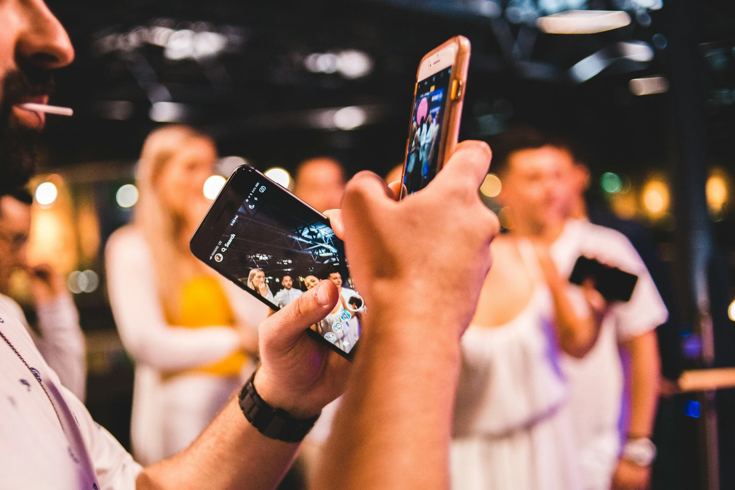 People taking photos with smartphones at a social gathering, with blurred background of other attendees.