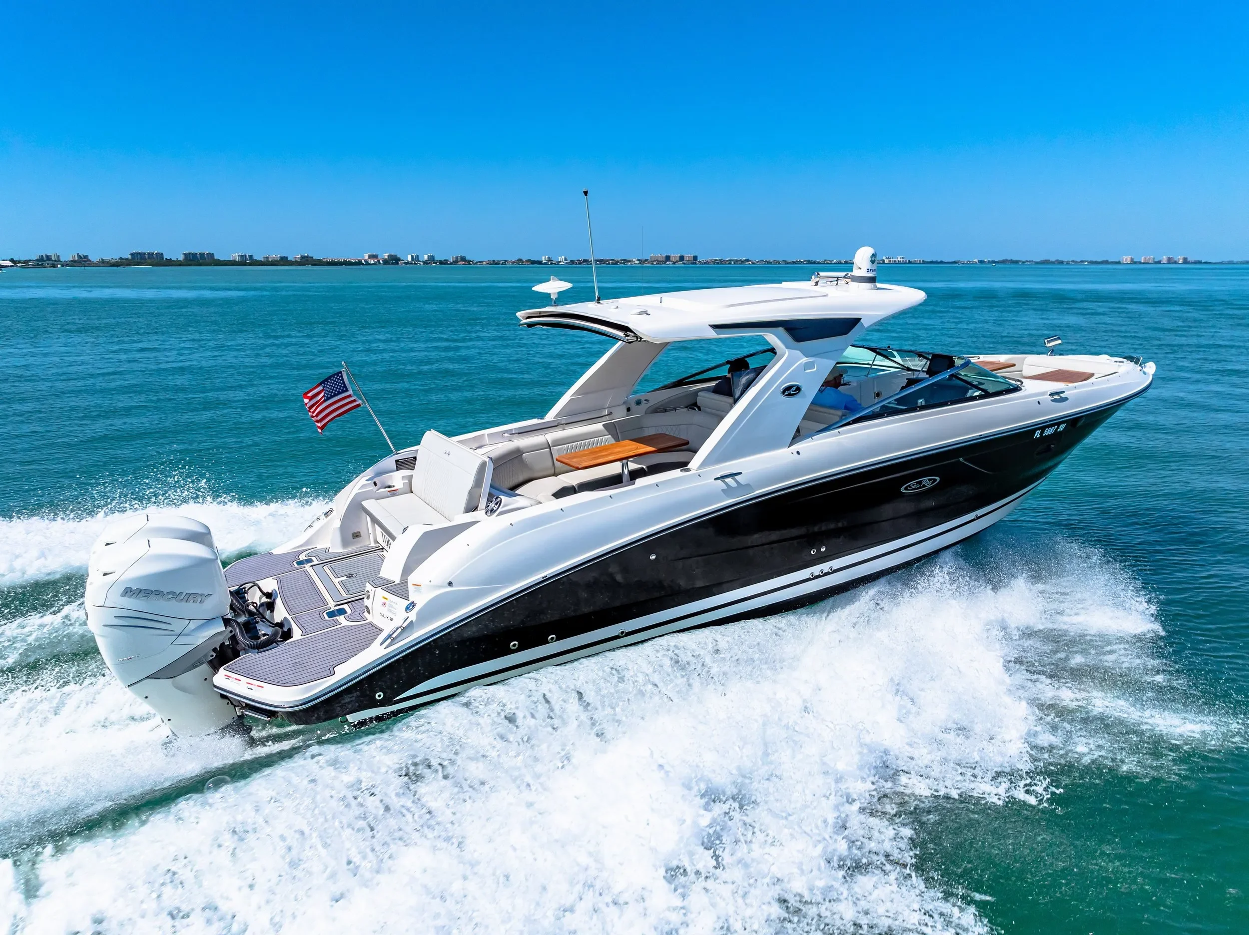 A white and black motor yacht speeding across blue water with a city skyline in the distance.
