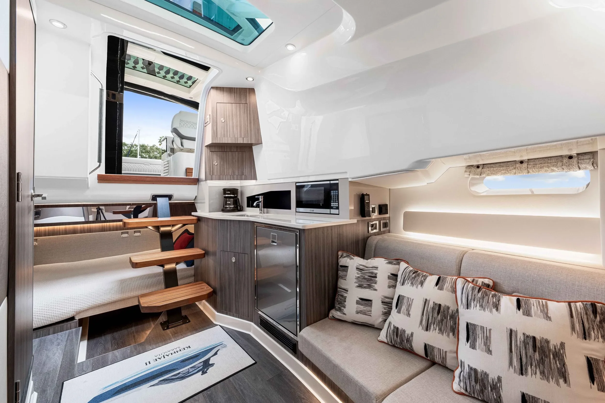 kokomo charters - 40' Golden Ticket - Interior of a modern yacht cabin with a sofa, pillows, mini fridge, microwave, coffee maker, small sink, and wood accents, with a window and a door leading outside.
