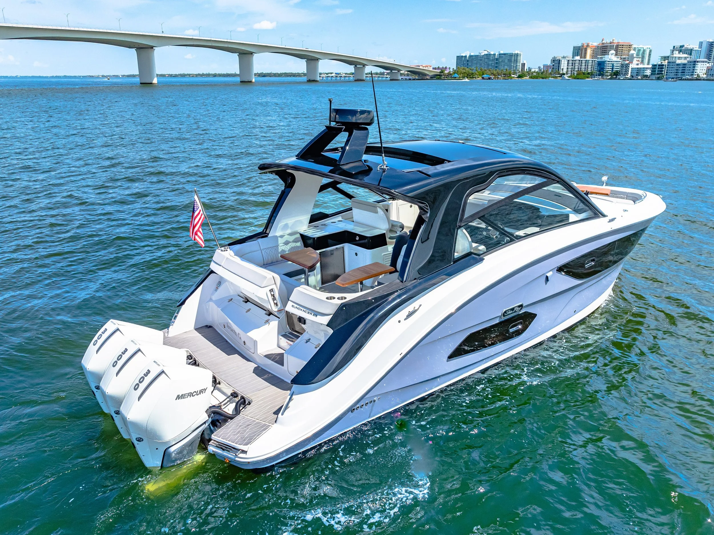 A white motor yacht cruising on a body of water with a city skyline and a bridge in the background.