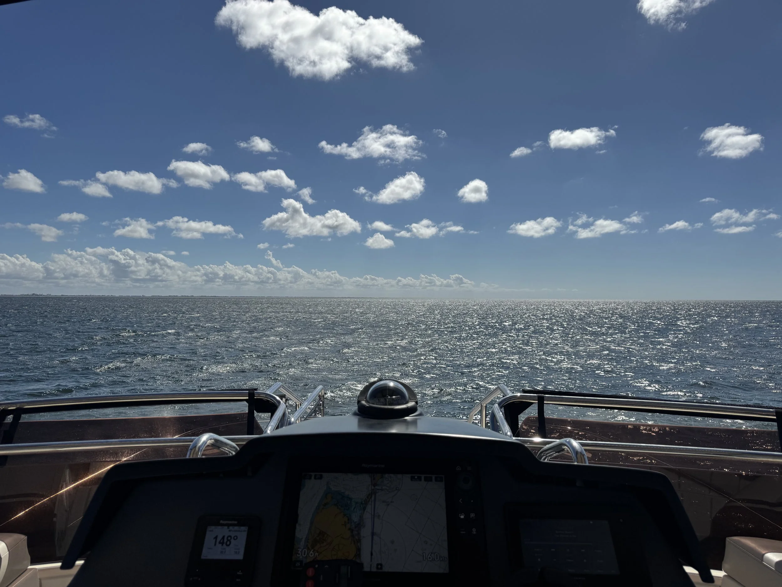 View from a boat's cockpit, with a sunny ocean horizon and partly cloudy sky.