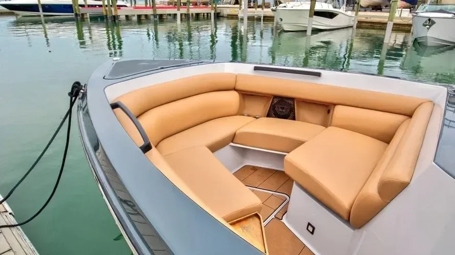 kokomo charters - 35' Ocean Rode - Interior of a boat with beige cushioned seating, docked at a marina with other boats and water in the background.