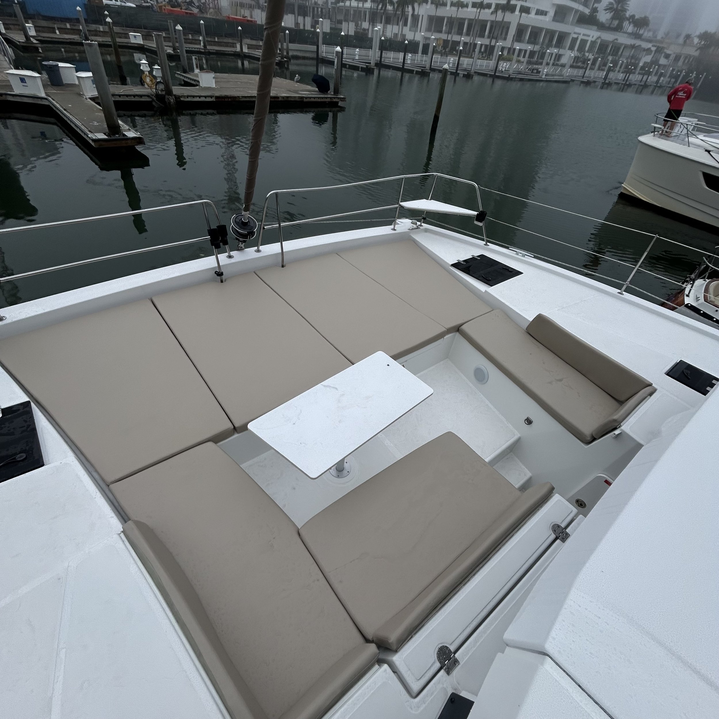 Boat deck with beige cushioned seating and a white table, dock in the background.
