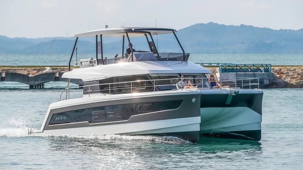 A modern luxury yacht cruising on calm water with people relaxing on the deck, distant land and mountains in the background.